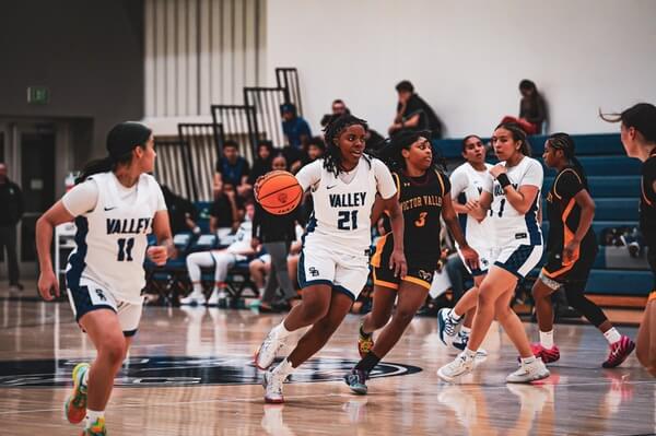 SBVC women's basketball player drives down the court during a game as teammates and defenders position themselves around the play.